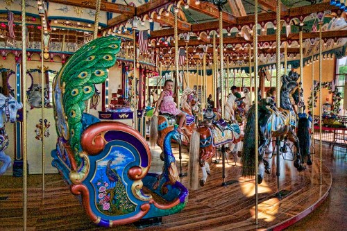 A colorful carousel with intricately designed horses and a girl riding, surrounded by festive decorations.