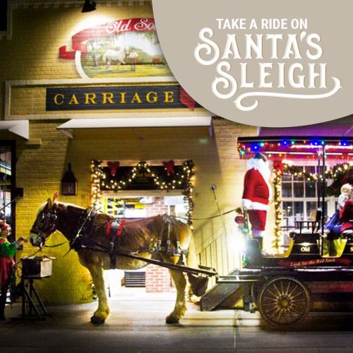A festive scene featuring a horse-drawn carriage with Santa and elves, decorated for the holidays outside a shop.