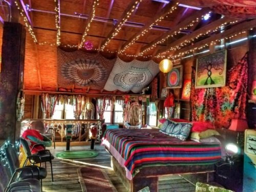Cozy, colorful bedroom with string lights, vibrant tapestries, and a large bed, creating a warm, inviting atmosphere.