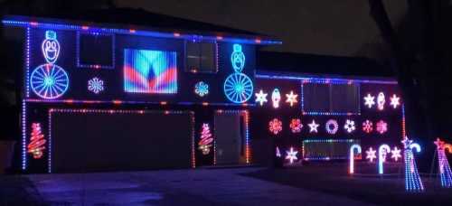 A house decorated with colorful Christmas lights, featuring snowmen, candy canes, and festive patterns.