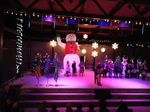 A large inflatable snowman stands on stage, surrounded by festive decorations and people in winter attire.