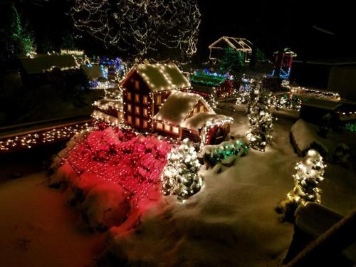 A snowy scene featuring a brightly lit house and decorated trees, surrounded by colorful holiday lights.