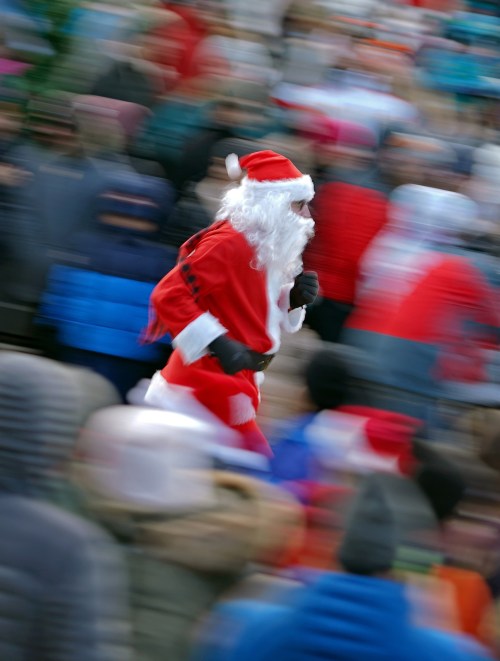 A blurred image of a person in a Santa costume running through a crowd during a festive event.