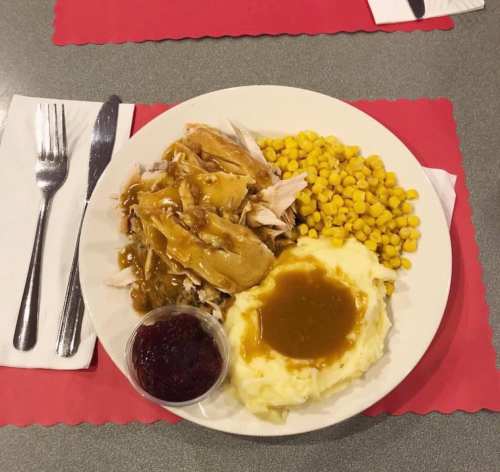 A plate of turkey with gravy, mashed potatoes, corn, and a side of cranberry sauce on a table setting.