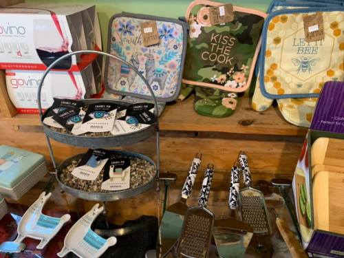 A display of kitchen items including pot holders, graters, and decorative accessories on a wooden shelf.
