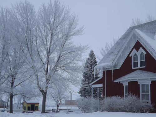 A snowy scene featuring a red house, frosted trees, and a colorful playhouse in the background.