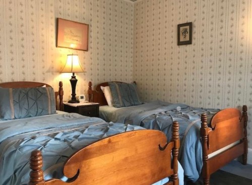 Cozy bedroom with two wooden twin beds, blue bedding, a lamp, and floral wallpaper.