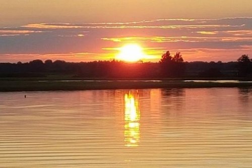 A serene sunset over a calm lake, with vibrant orange and yellow hues reflecting on the water's surface.