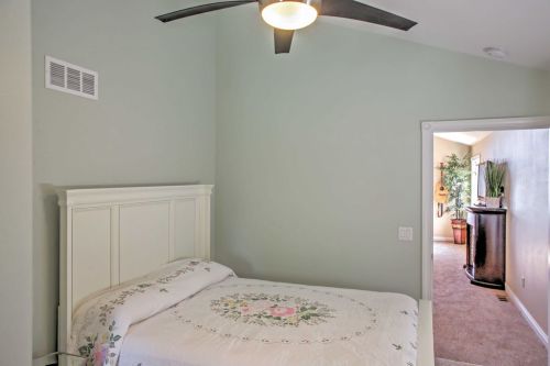 Cozy bedroom with a white bed, floral bedding, and a ceiling fan, leading to a hallway with plants and decor.