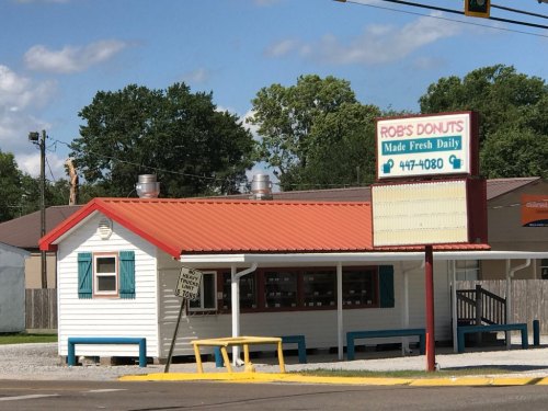 A small, white donut shop with a red roof and blue accents, featuring a sign that reads "Rob's Donuts" and a phone number.