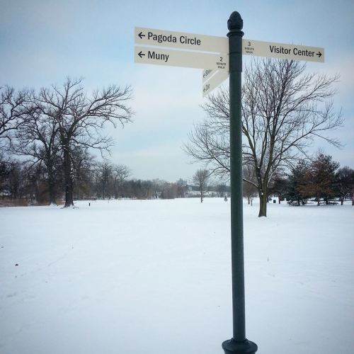 A signpost in a snowy park, pointing to Pagoda Circle, Muny, and Visitor Center, with bare trees in the background.