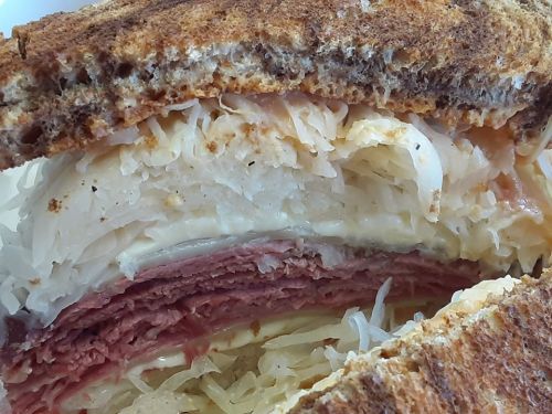 Close-up of a layered sandwich with corned beef, sauerkraut, and melted cheese between slices of toasted rye bread.