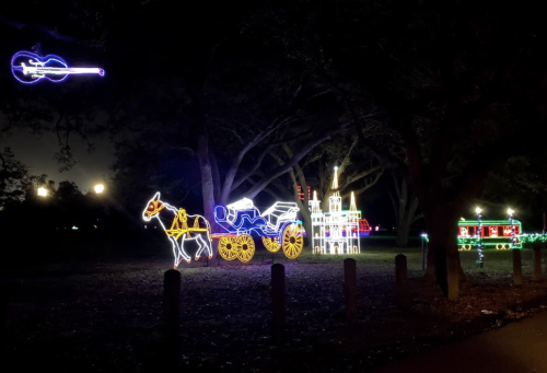 Colorful holiday lights depicting a horse-drawn carriage, a castle, and a train in a dark park setting.