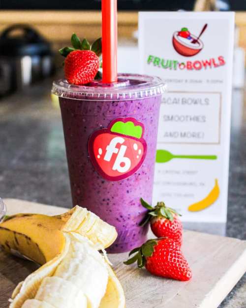 A smoothie in a cup with a strawberry logo, surrounded by a banana and strawberries, with a menu in the background.