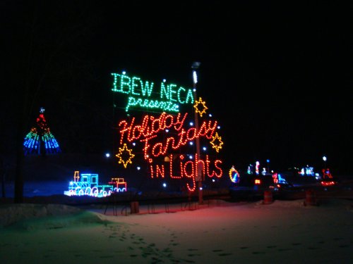 Colorful holiday lights display with the text "IBEW NECA presents Holiday Fantasy in Lights" against a dark night sky.