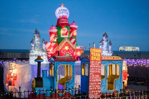 A colorful inflatable Christmas display featuring a candy castle and a train, illuminated with festive lights.