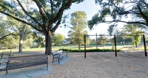 A peaceful park scene featuring benches, swings, and lush trees under a clear blue sky.
