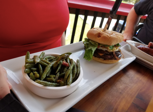 A plate featuring a burger with lettuce and a knife, alongside a bowl of green beans.