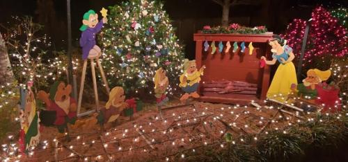 Colorful holiday scene featuring Snow White and the Seven Dwarfs by a decorated tree and lights.