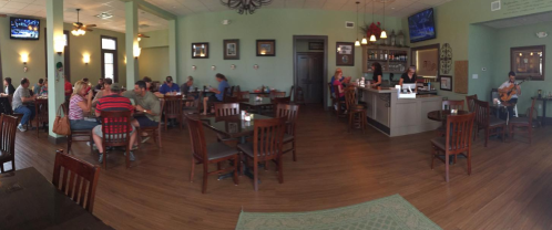 A cozy restaurant interior with diners at tables, a bar area, and a musician playing guitar in the background.