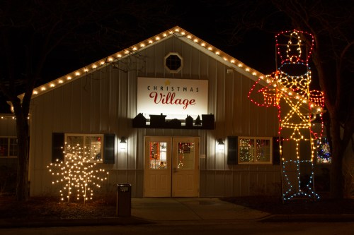 A festive building with a sign reading "Christmas Village," adorned with lights and a large nutcracker decoration.
