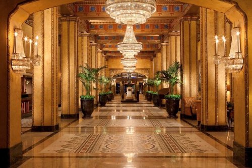 Luxurious hotel lobby with ornate chandeliers, golden walls, and lush plants, creating an elegant atmosphere.
