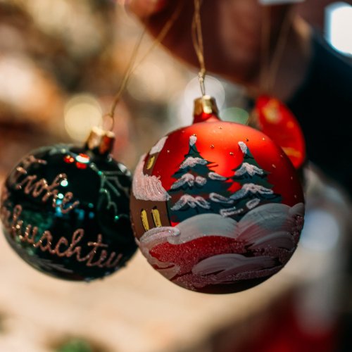 Two decorative Christmas ornaments: one green with "Evoke Schwacht" and one red featuring snowy trees and a cozy house.