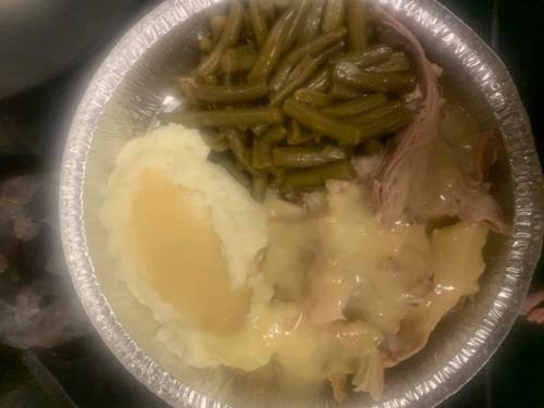 A foil tray filled with mashed potatoes, green beans, and sliced meat with gravy.