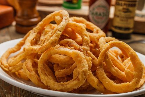 A plate piled high with crispy, golden-brown onion rings, served with condiments in the background.