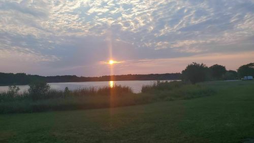 A serene sunset over a lake, with clouds reflecting warm colors and lush greenery in the foreground.