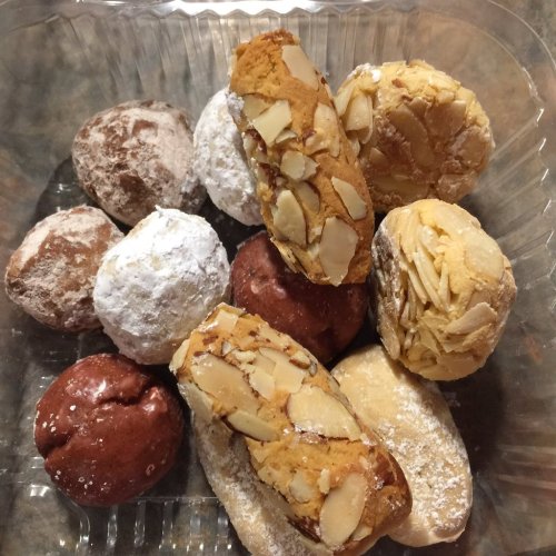 A variety of cookies, including powdered, almond-topped, and chocolate-flavored, arranged in a clear container.