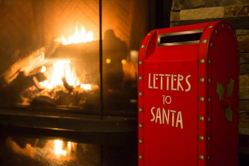 A red mailbox labeled "Letters to Santa" stands near a cozy fireplace with a warm glow.