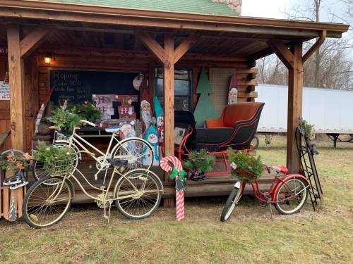 A rustic cabin porch decorated with vintage bicycles, a sleigh, and festive greenery for the holiday season.