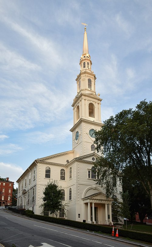 A historic church with a tall golden steeple, surrounded by trees and a clear blue sky.