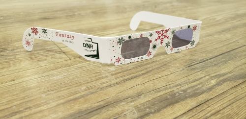 White 3D glasses with festive designs, featuring snowflakes and the text "Fantasy" and "DNR" on the sides, resting on a wooden surface.