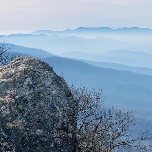 A rocky outcrop in the foreground with layered blue mountains fading into the distance under a soft sky.