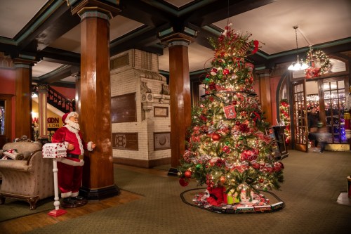 A festive lobby decorated for Christmas, featuring a large tree and a Santa figure beside a cozy armchair.