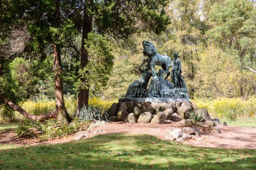 A bronze statue of a lion on a rocky base, surrounded by trees and greenery in a park setting.