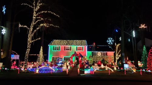 A brightly lit house decorated with colorful Christmas lights, inflatables, and festive ornaments in a nighttime setting.