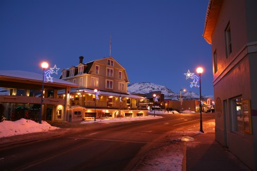 A snowy street scene at dusk, featuring a lit-up building and festive decorations along the road.