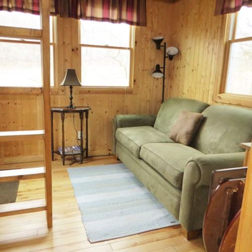 Cozy wooden interior with a green sofa, a small table with a lamp, and a staircase leading to another level.