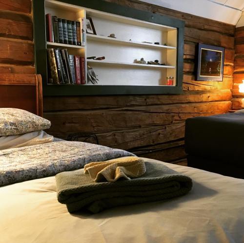 Cozy cabin interior with a bed, neatly folded towels, and a shelf displaying books and decorative items. Warm lighting.