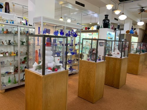 A brightly lit antique shop featuring glass display cases filled with colorful glassware and decorative items.