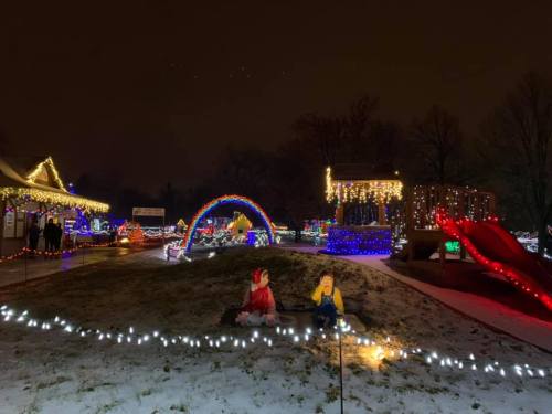 Colorful holiday lights illuminate a snowy park scene with decorations, a rainbow arch, and playful figures.