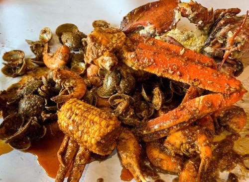 A vibrant seafood platter featuring crab, shrimp, clams, and corn, all coated in a spicy sauce.