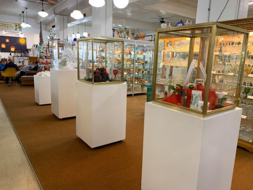 A spacious antique shop featuring display cases with various collectibles and glassware, set on a carpeted floor.