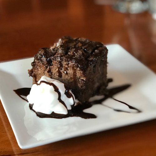 A slice of chocolate cake topped with whipped cream and drizzled with chocolate sauce on a white plate.