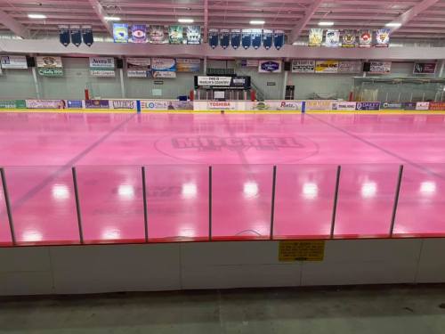 A hockey rink with a bright pink ice surface and colorful banners hanging in the background.