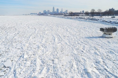A snowy landscape with ice formations, overlooking a city skyline in the distance under a clear sky.