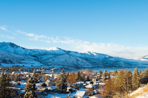 A snowy landscape with a small town, mountains in the background, and a clear blue sky.